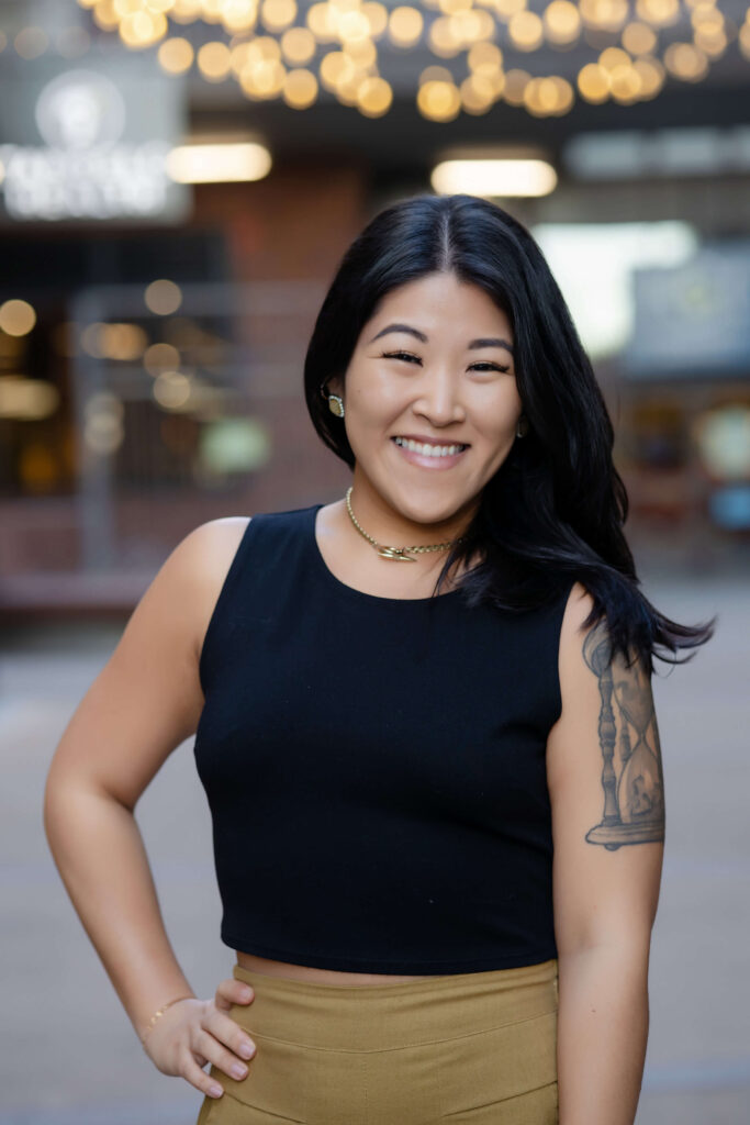 Woman smiles boldly in headshot wearing a black tank top with bokeh background